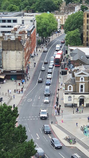 A street scene in Harlesden featuring a large, historic brick building with a prominent arched window on the upper floor, and a modern railway bridge with yellow and green signage reading 'Camden Lock